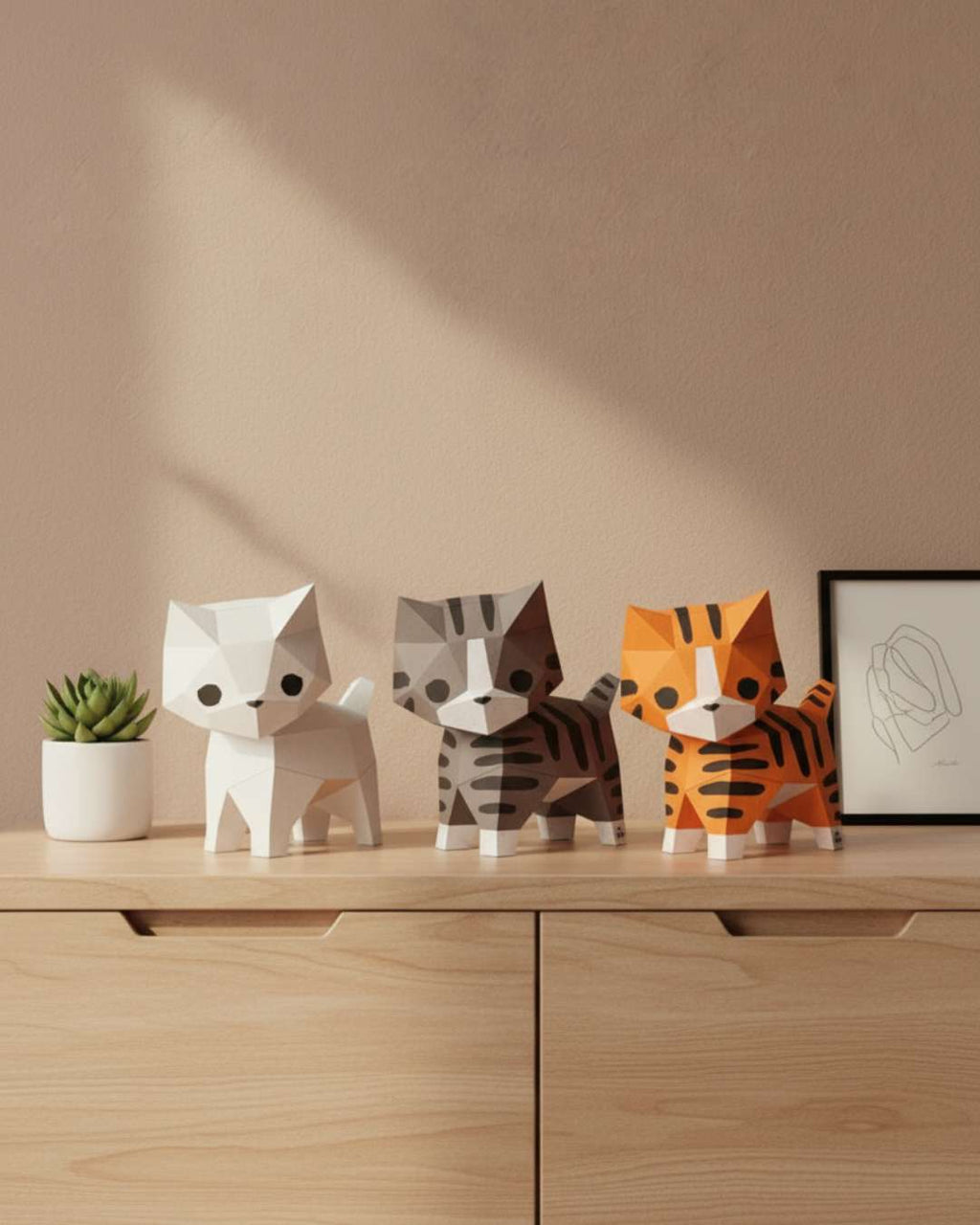 Trois chats décoratifs en papier Moki Moki — blanc, tigré gris et roux — posés sur une commode en bois clair, dans une mise en scène douce et minimaliste.