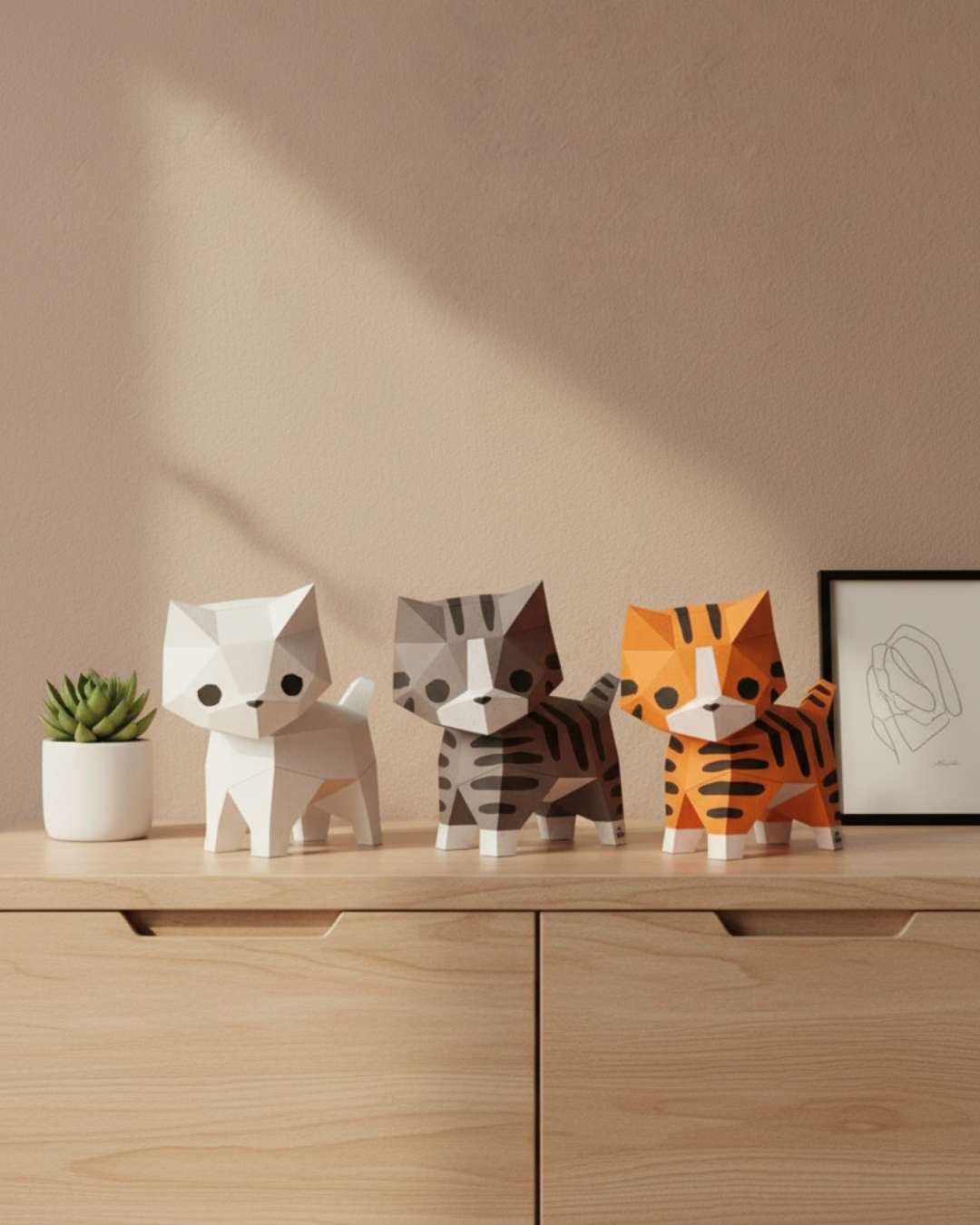 Trois chats décoratifs en papier Moki Moki — blanc, tigré gris et roux — posés sur une commode en bois clair, dans une mise en scène douce et minimaliste.