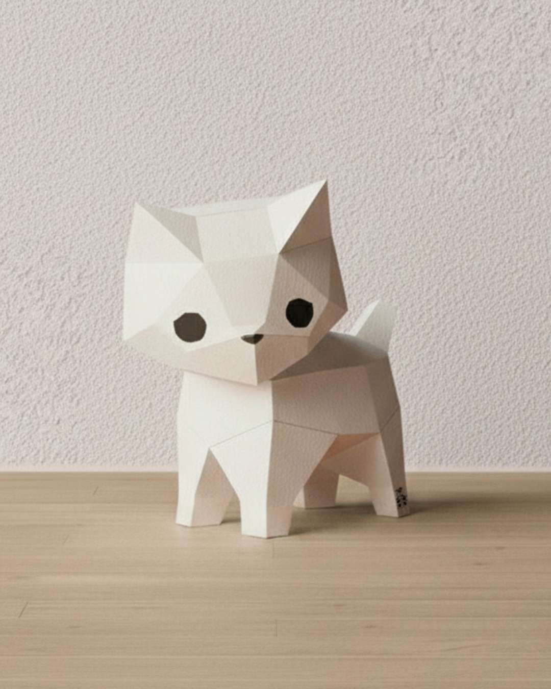 Chat blanc en papercraft 3D Moki Moki, figurine de style origami en papier à monter soi-même, posé sur un sol en bois clair devant un mur texturé.