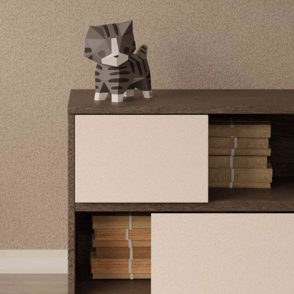 Le papercraft chaton est sur une commode dans la chambre d'un enfant. Le chat est entouré d'autres créations de style origami 3D de Moki Moki.