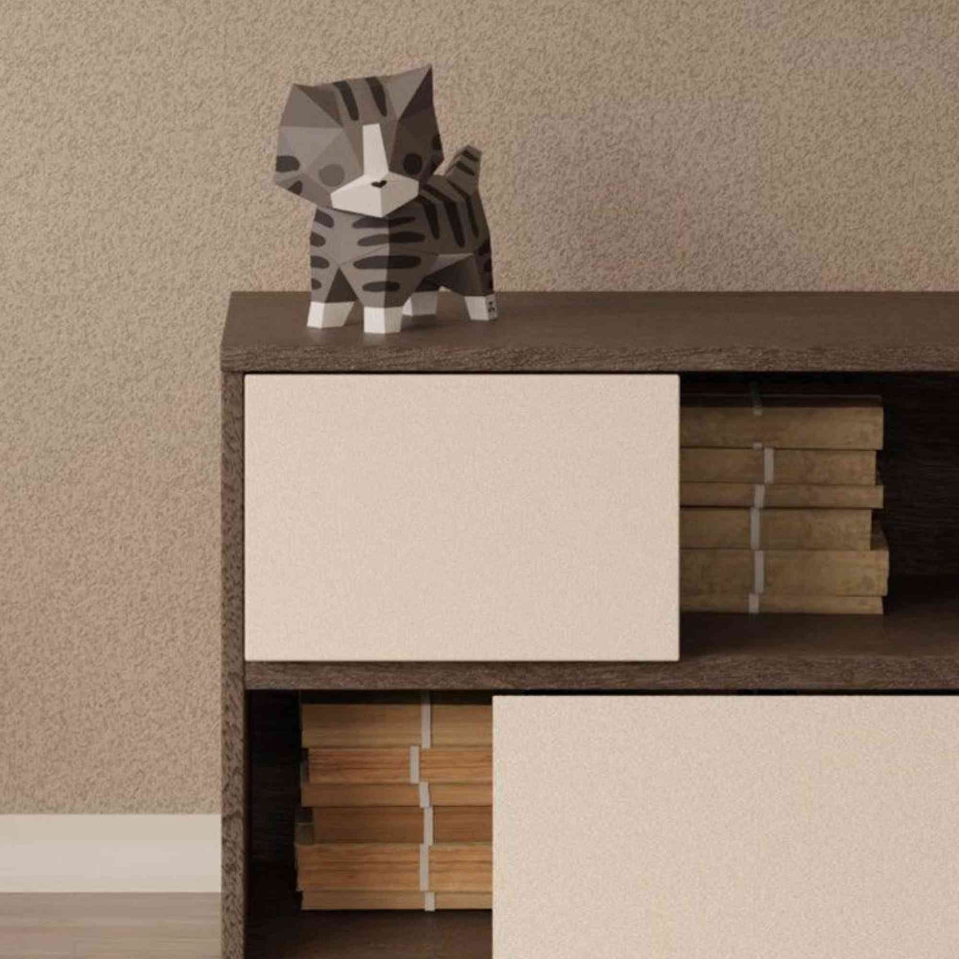 Le papercraft chaton est sur une commode dans la chambre d'un enfant. Le chat est entouré d'autres créations de style origami 3D de Moki Moki.
