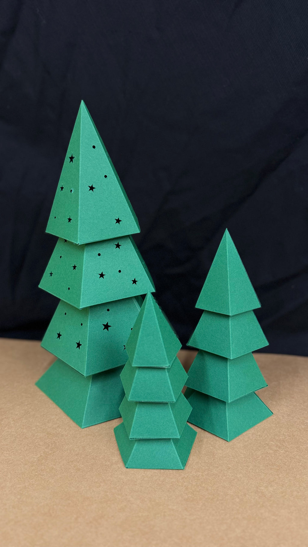 Sapin de Noël en papercraft 3D perforé d’étoiles, présenté avec deux sapins décoratifs assortis.
