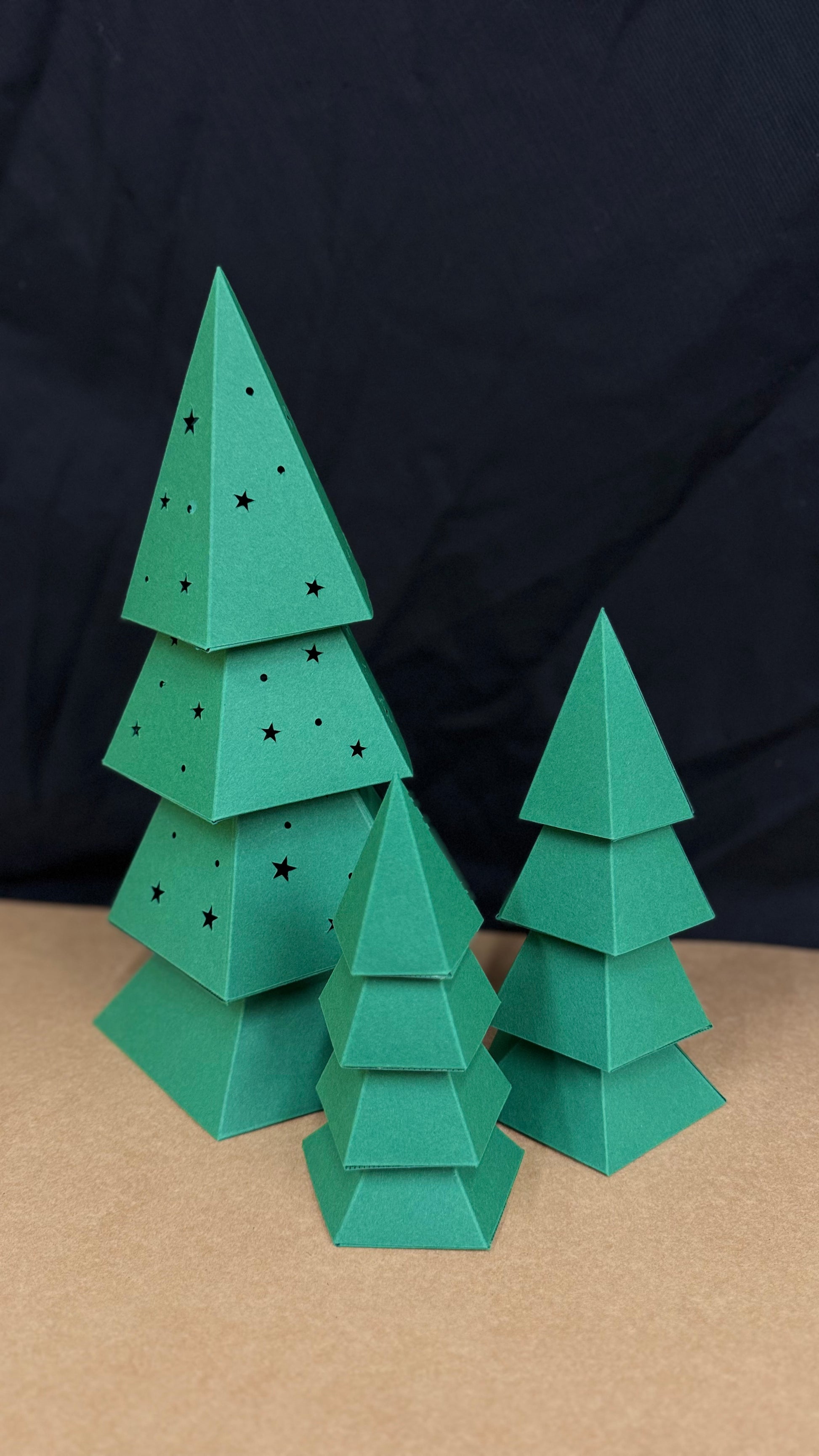 Sapin de Noël en papercraft 3D perforé d’étoiles, présenté avec deux sapins décoratifs assortis.