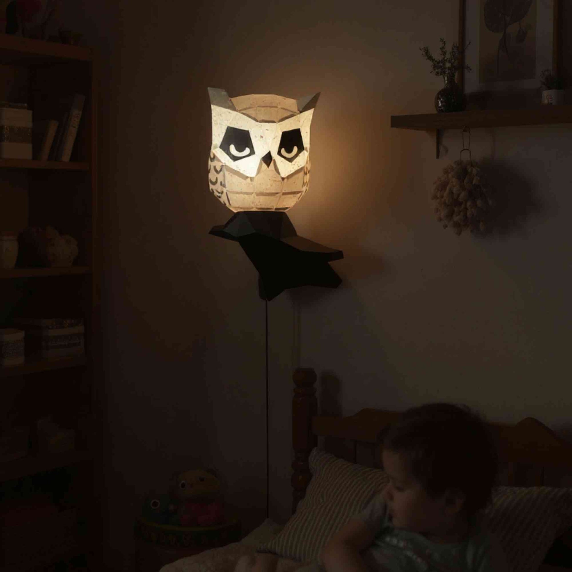 La lampe applique murale hibou en papier style origami 3D est perché sur sa branche dans une chambre de bébé. La veilleuse est allumée et révèle la couleur naturelle de cet animal de la forêt. L'éclairage de ce wall art est doux et parfait pour des nuits paisibles.