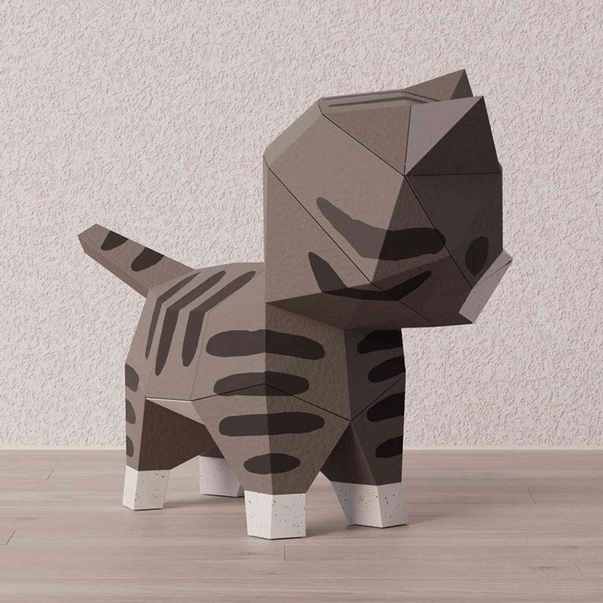 Papercraft 3D d'un petit chat en style origami. On voit le chaton réalisé en papier vu de dos. L'animal est de couleur naturelle.