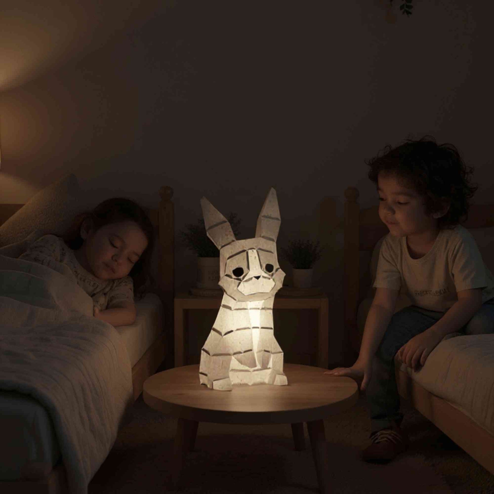 La veilleuse bébé et enfant lapin en papier style origami 3D est sur la table de chevet dans une chambre de petits enfants. Les deux petites filles sont en train de s'endormir. La veilleuse est allumée et révèle la couleur naturelle grise du lapin. L'éclairage est doux et parfaite pour des nuits tranquilles et apaisées.